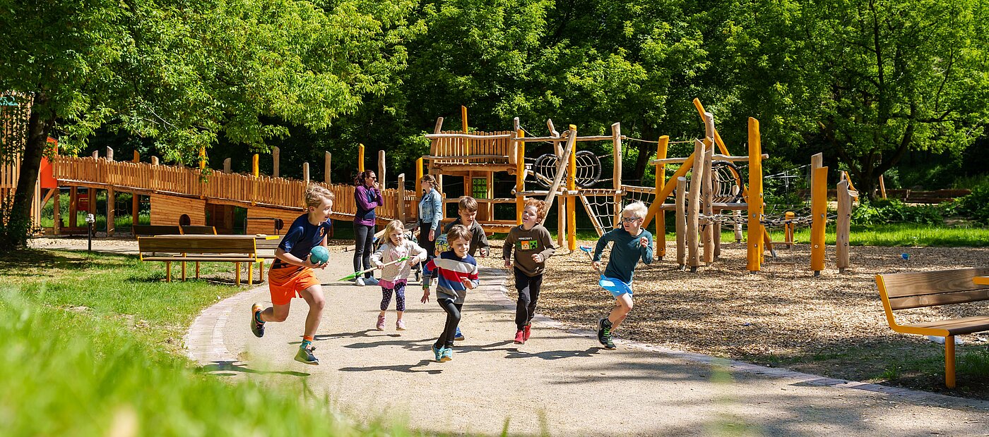 Kinder rennen vor dem Klettergerüst mit Ball in der Hand