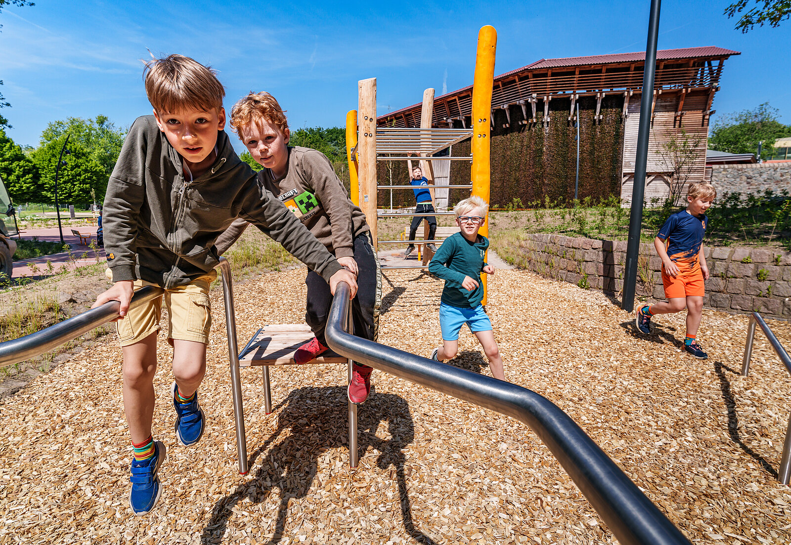 Zwei Kinder sitzen auf einem Klettergerüst im Hintergrund spielen weitere Kinder im Sand