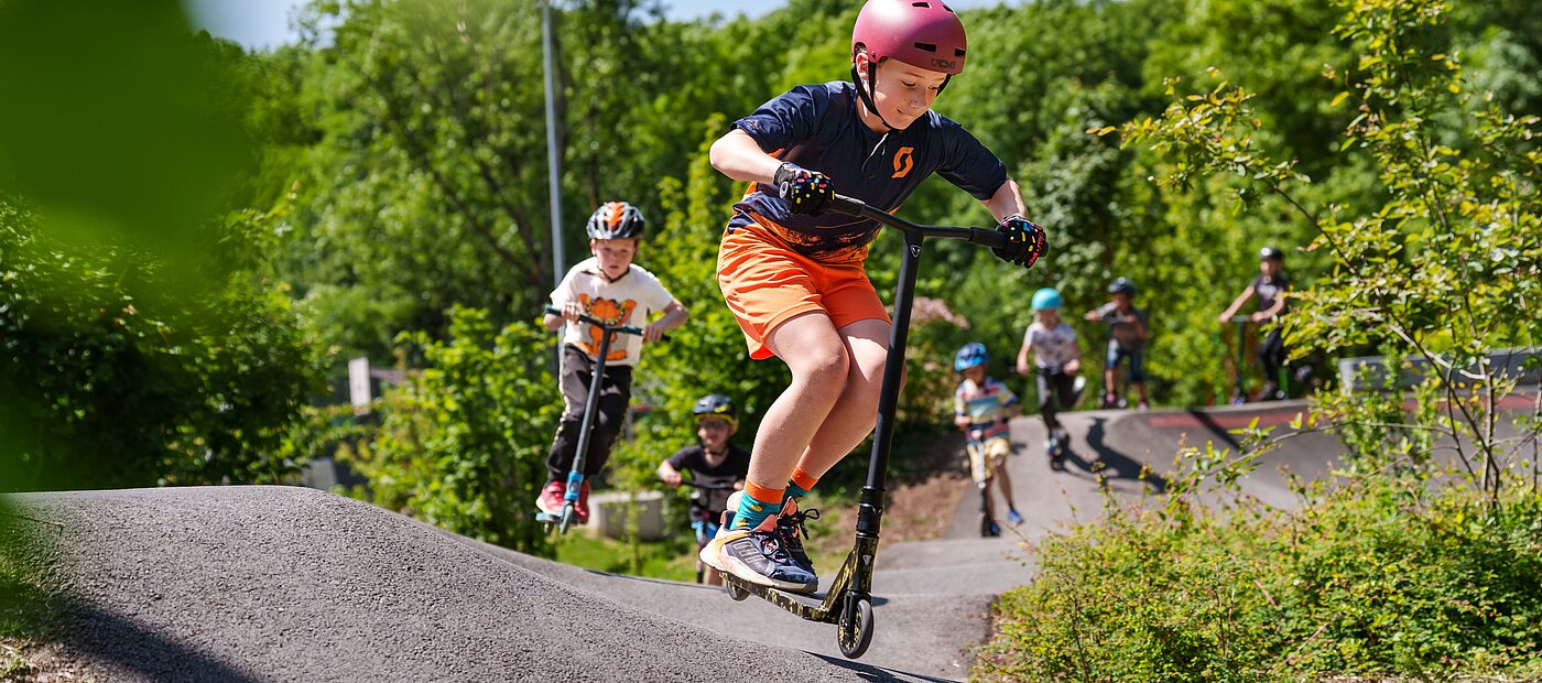 Kleine Jungs mit  Helm fahren auf Rollern den Pumptrack