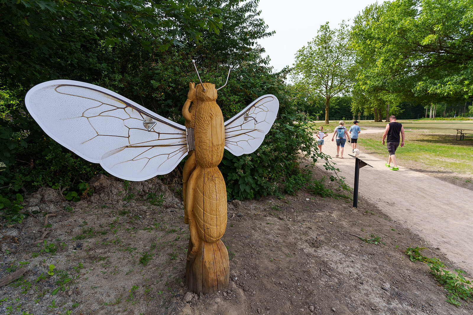 Auf dem Foto sieht man den Start des Bienen-Loops mit einer Holz-Skulptur einer Biene, deren Flügel Besuchende bewegen können.